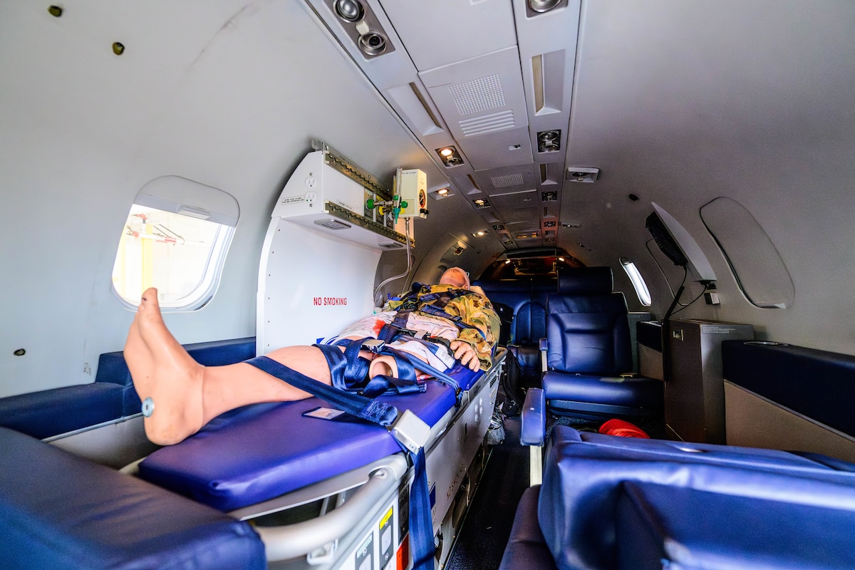 A medical dummy sits in a bed inside of a small jet. The dummy is surrounded by medical equipment.