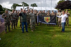 Retired U.S. Army Col. Paul Herbert (left), former executive director of the First Division Museum at Cantigny Park, U.S. Army Lt. Col. Brian Ault (center), cyber operations officer for the 1st Infantry Division, and Pierre Gosselin (right), owner of the Big Red One Assault Museum in Colleville-sur-Mer, France, pose for a photo with Soldiers in Colleville-sur-Mer, France, June 2, 2026. Ault presented Gosselin with a flag of the 1st Infantry Division in recognition of his work preserving the history and legacy of Soldiers who fought during the D-Day invasion at Omaha Beach. (U.S. Army photo by Sgt. Joshua Fish)