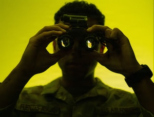 U.S. Air Force Staff Sgt. Jonathan Fuentes-Ayala, 6th Operation Support Squadron, aircrew flight equipment craftsman, peers through night vision goggles at MacDill Air Force Base, Florida, May 19, 2026. Night vision equipment is maintained and inspected by AFE technicians to support aircrew mission capabilities in low-light environments. (U.S. Air Force photo illustration by Airman Micquill Davis)