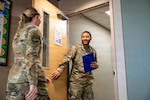 Uniformed service member holds binder and opens door for another service member