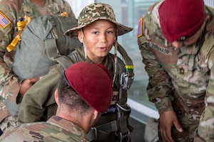 U.S. Army 1st Lt. Jeremy Shepler, left, a logistics officer assigned to the Light Support Battalion, 173rd Airborne Brigade, assists a student from Picauville Elementary School with a parachute harness during a D-Day 82 exchange at Picauville, France, June 2, 2026. The 173rd Airborne Brigade joined representatives from the Golden Knights and the Round Canopy Parachute Team to orient French school children to paratrooper equipment. (U.S. Army photo by Maj. Joe Legros)