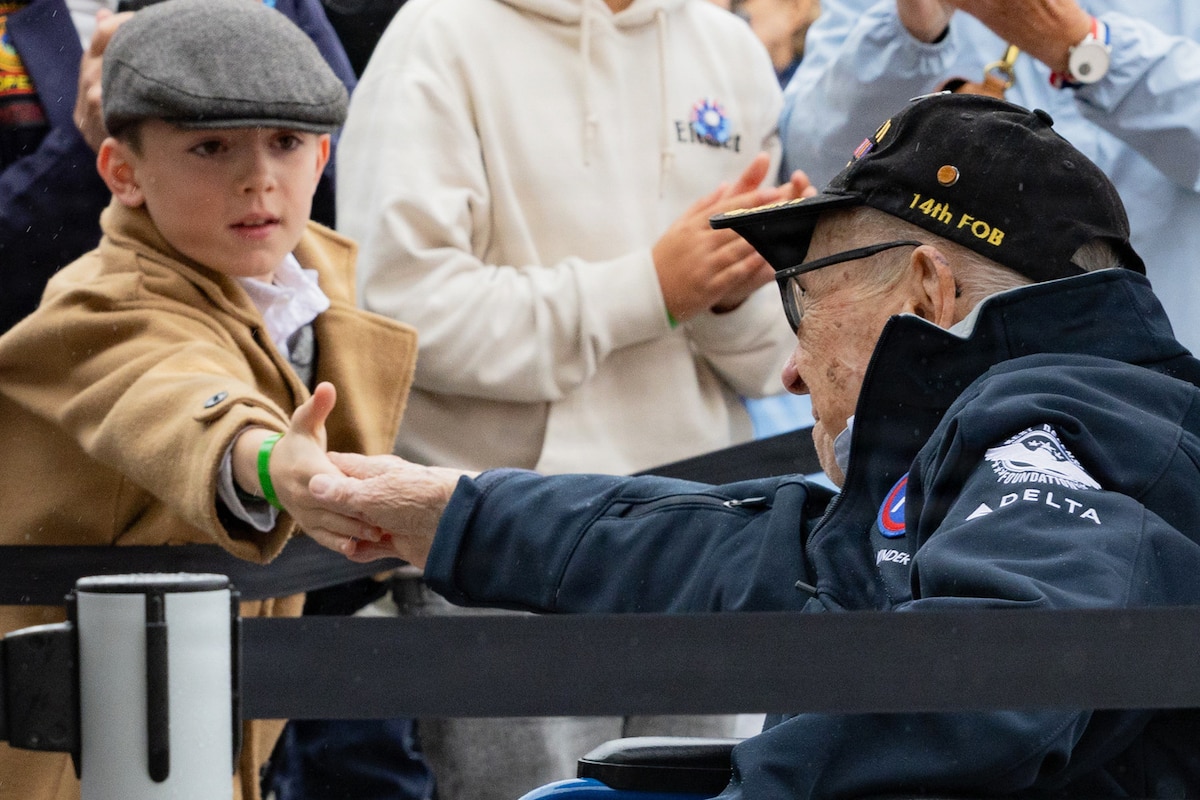 A veteran using a wheelchair shakes hands with a child among a crowd.