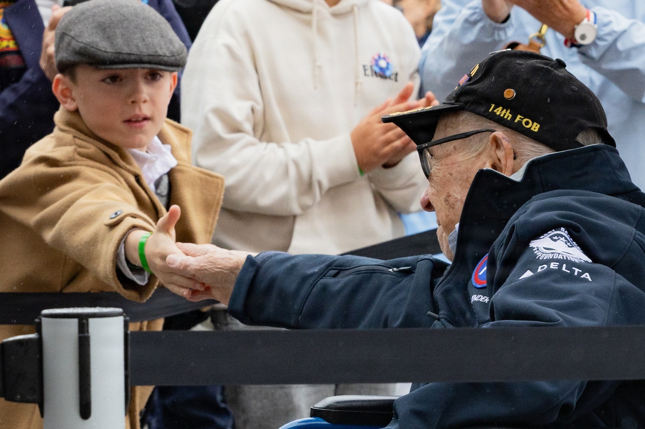 A veteran using a wheelchair shakes hands with a child among a crowd.