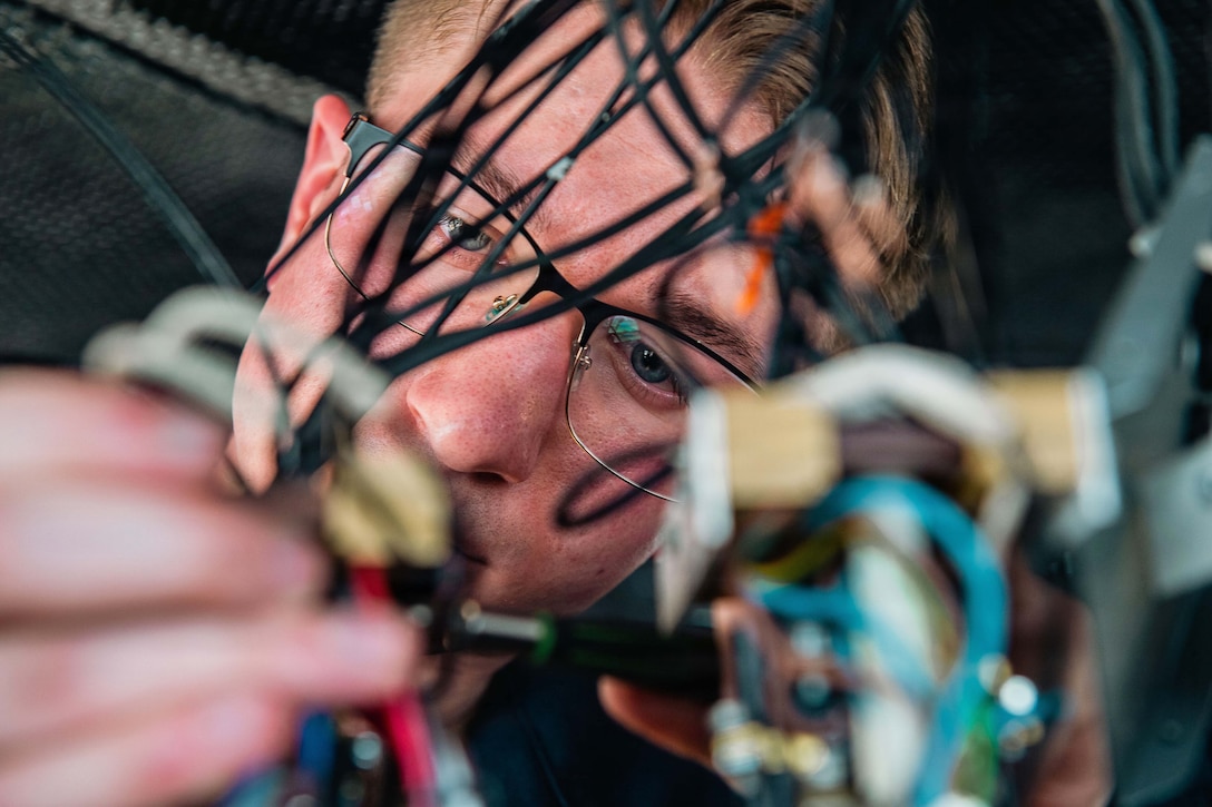 A close-up of a sailor wearing glasses connecting wires.