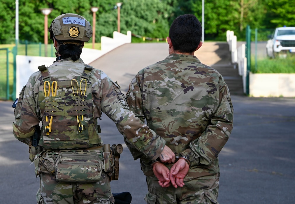 A U.S. Air Force security forces airman escorts another airman out of a building.