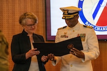 U.S. Coast Guard outgoing commander and director of Operational Logistics Command reading over a certificate.