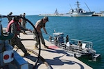 Sailors pull on a rope from a boat.