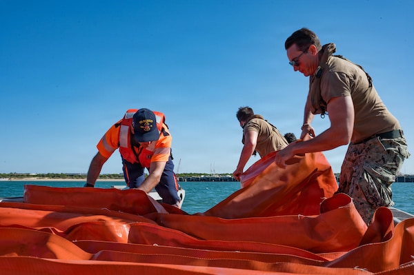 Sailors and local nationals unravel an orange inflatable boom.