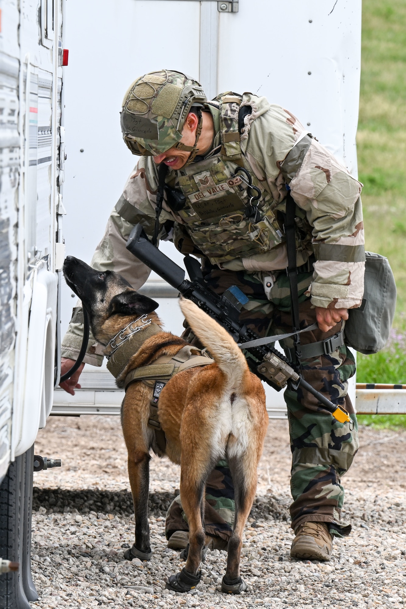 Airman in camouflage gear directs a military working dog during a field operation.