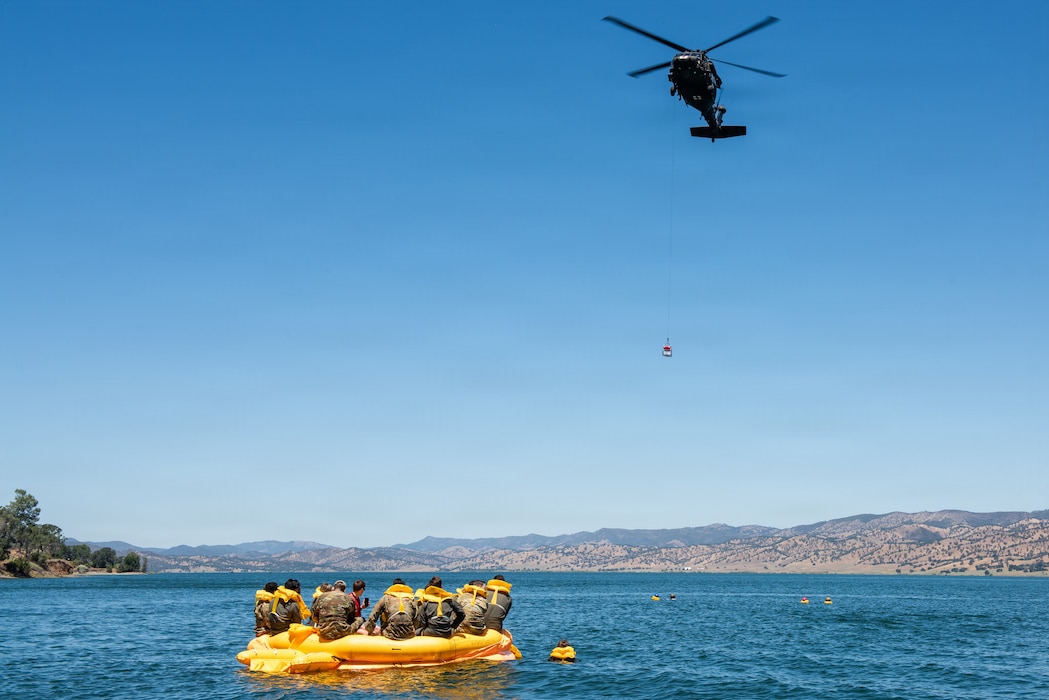 Helicopter lowers rescue basket with Airmen in life raft in the foreground