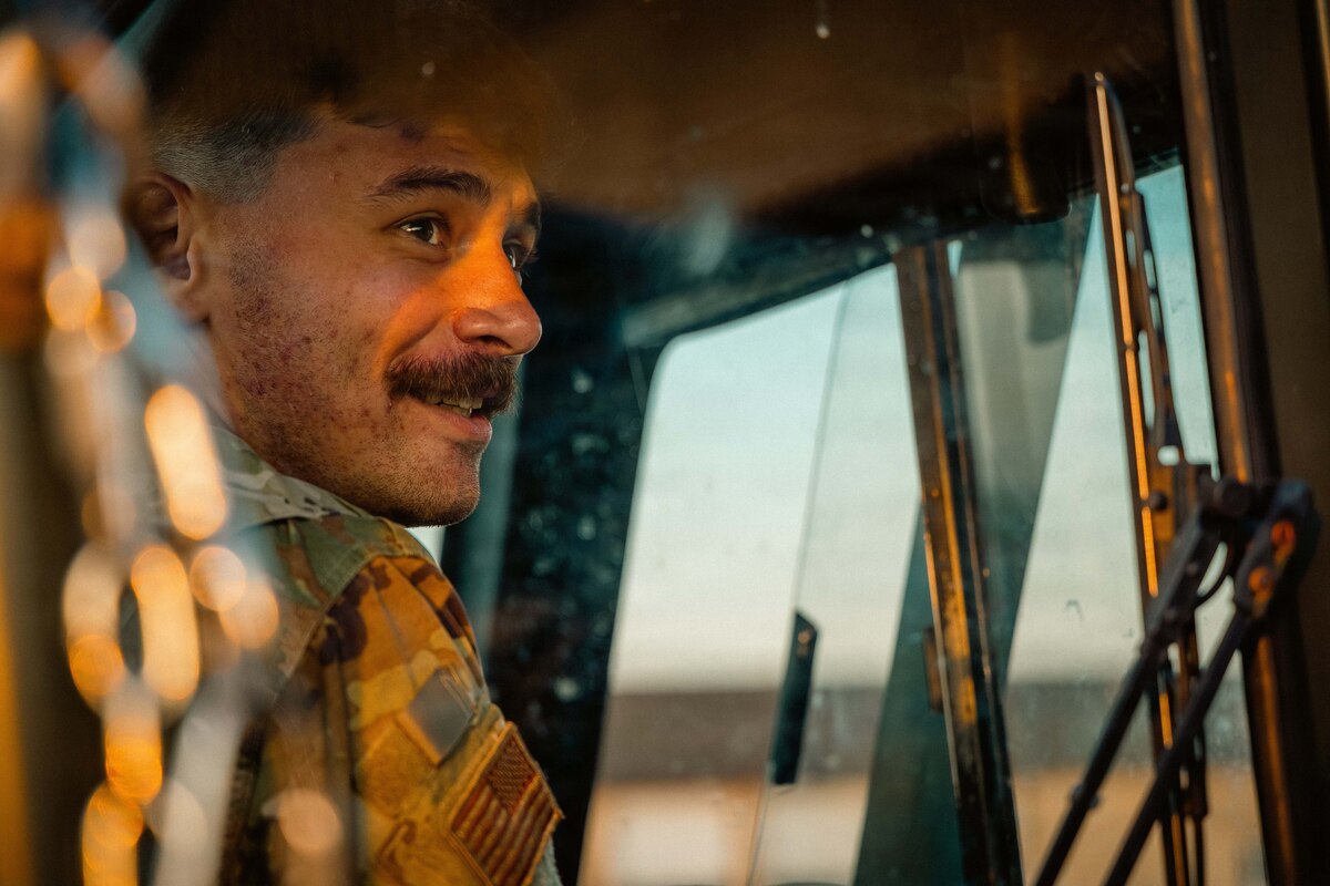 A man in a camouflage military uniform looks out the window of a military loading vehicle.
