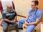 Patient sits on exam table talking to a seated doctor.