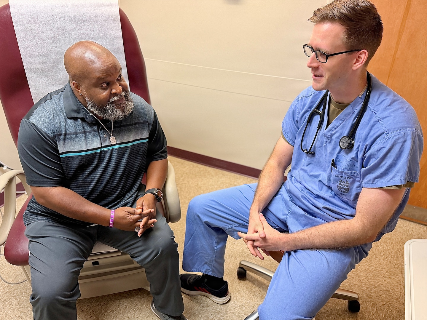 Patient sits on exam table talking to a seated doctor.