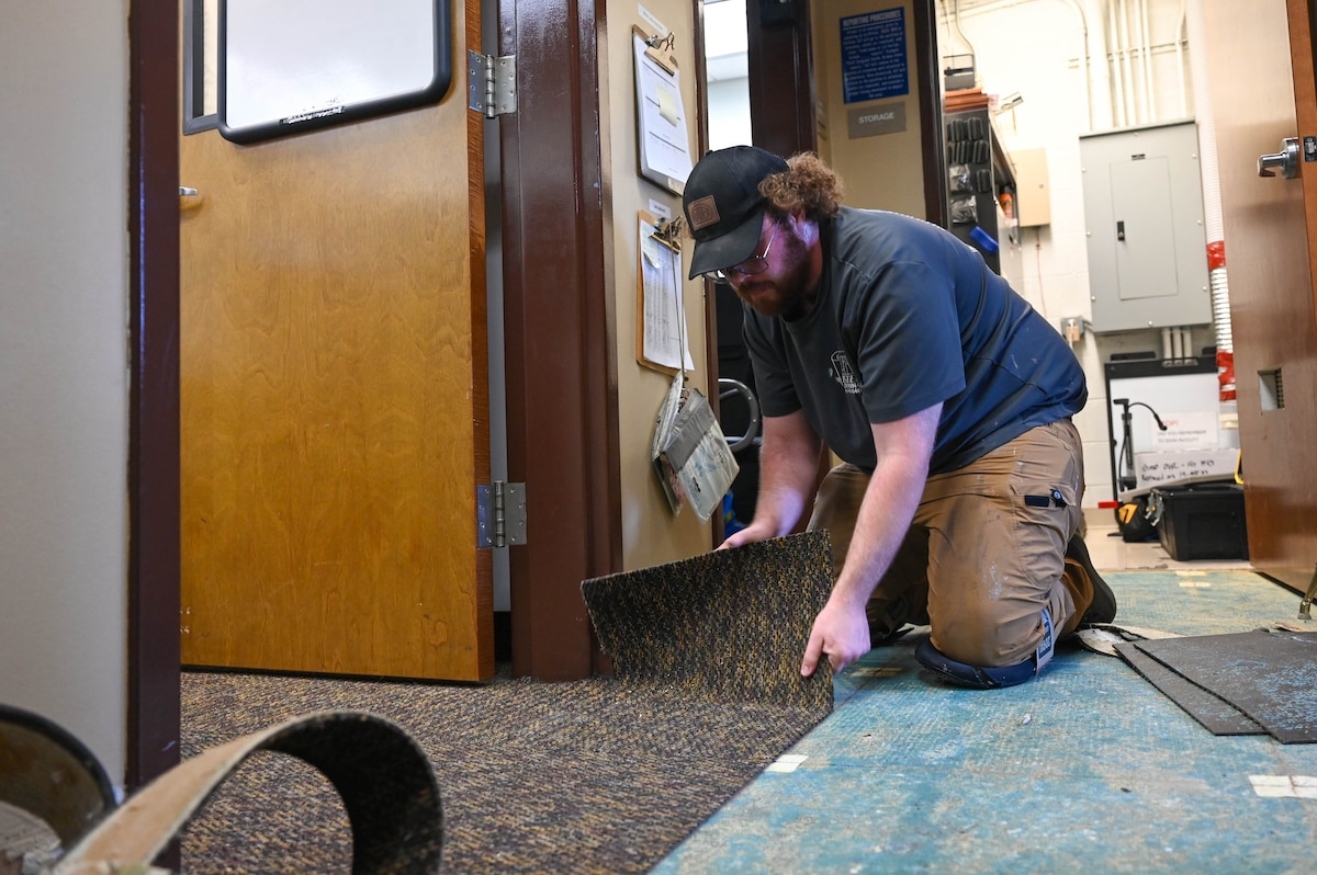 A man pulls up a carpet tile.