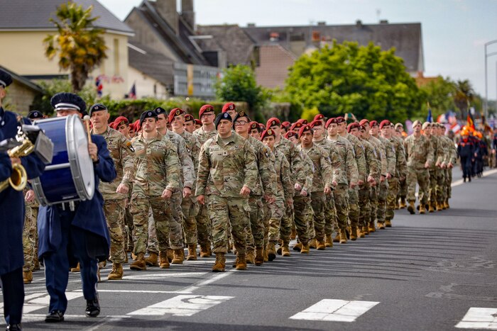 Soldiers in uniform walk in formation on a town street.
