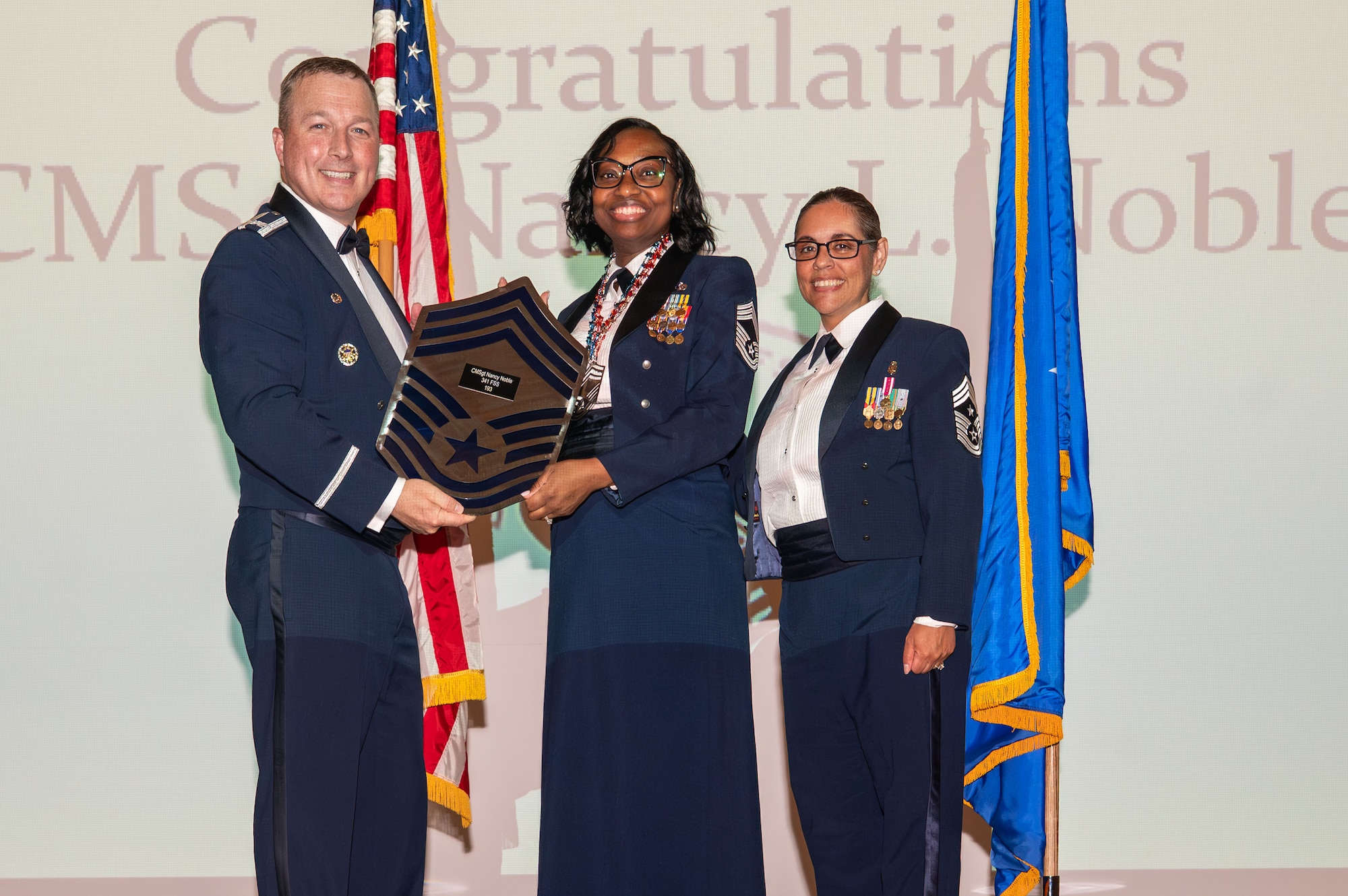 U.S. Air Force Chief Master Sgt. Nancy Noble, 341st Force Support Squadron senior enlisted leader, center, receives a plaque from Col. Daniel Voorhies, 341st Missile Wing commander, in recognition of her advancement to the pinnacle of the enlisted rank structure, during the 2026 Chief Master Sgt. recognition ceremony at Malmstrom Air Force Base, Montana, May 29, 2026.