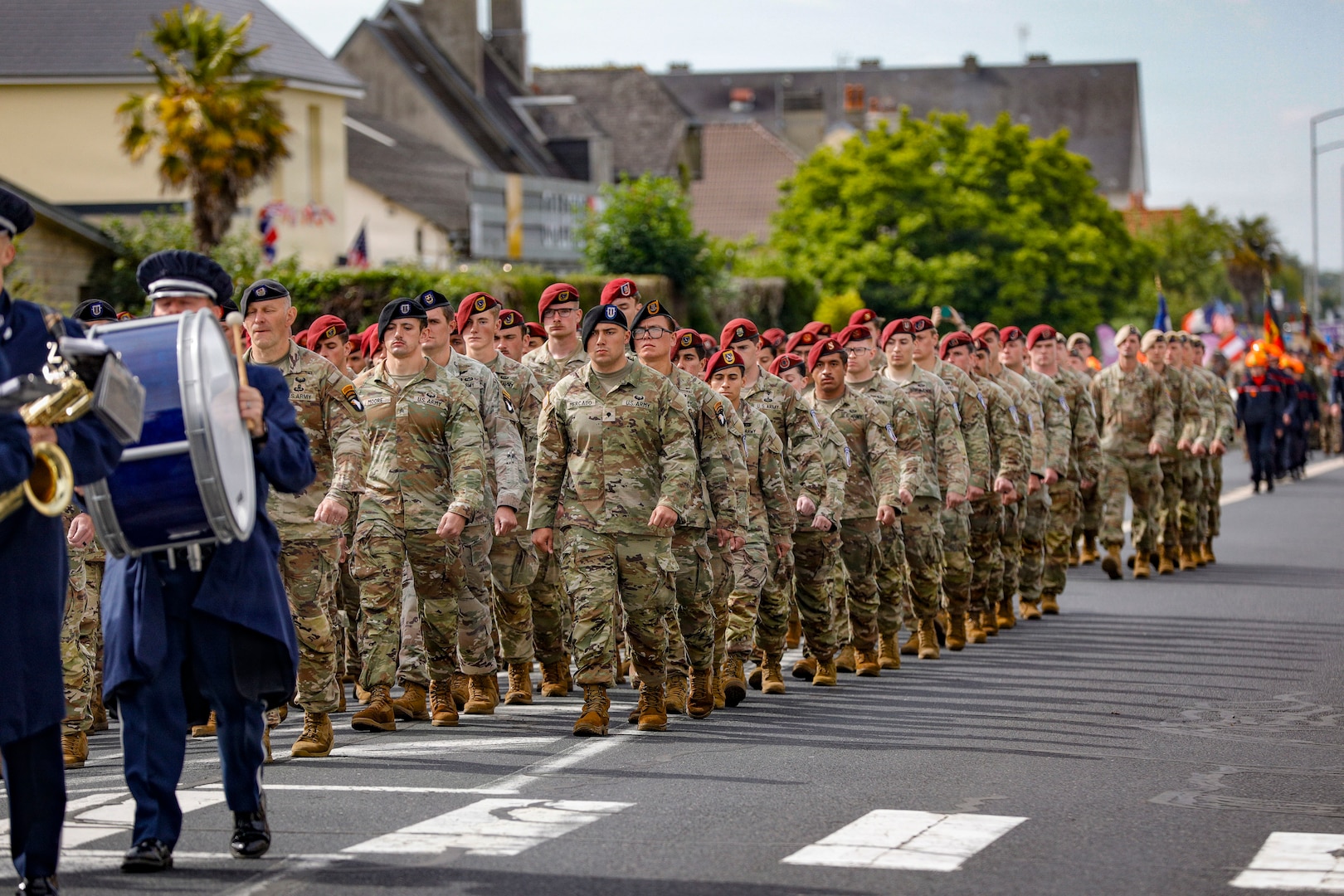 Soldiers in uniform walk in formation on a town street.