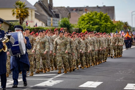 Soldiers in uniform walk in formation on a town street.