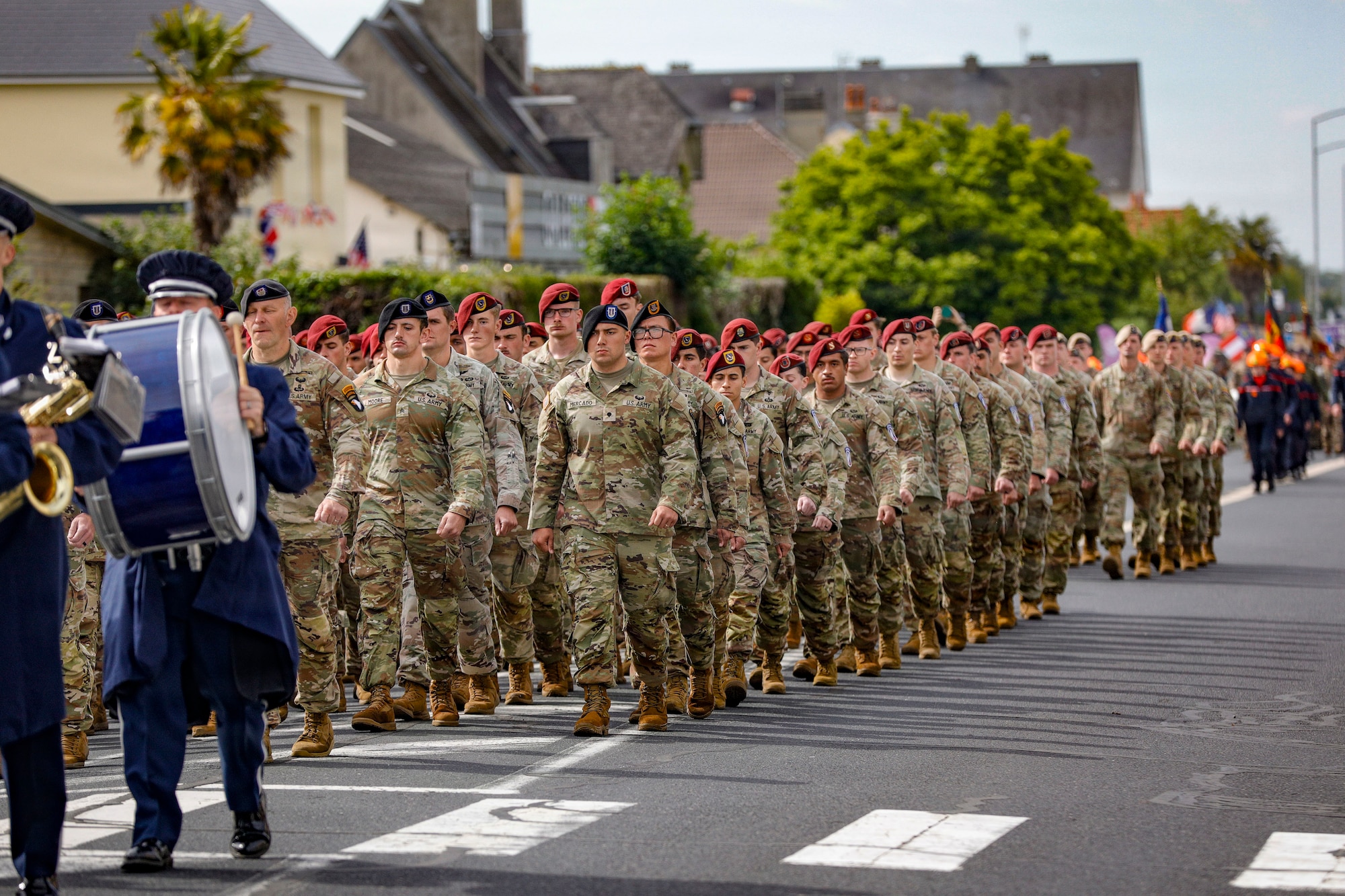 Soldiers in uniform walk in formation on a town street.