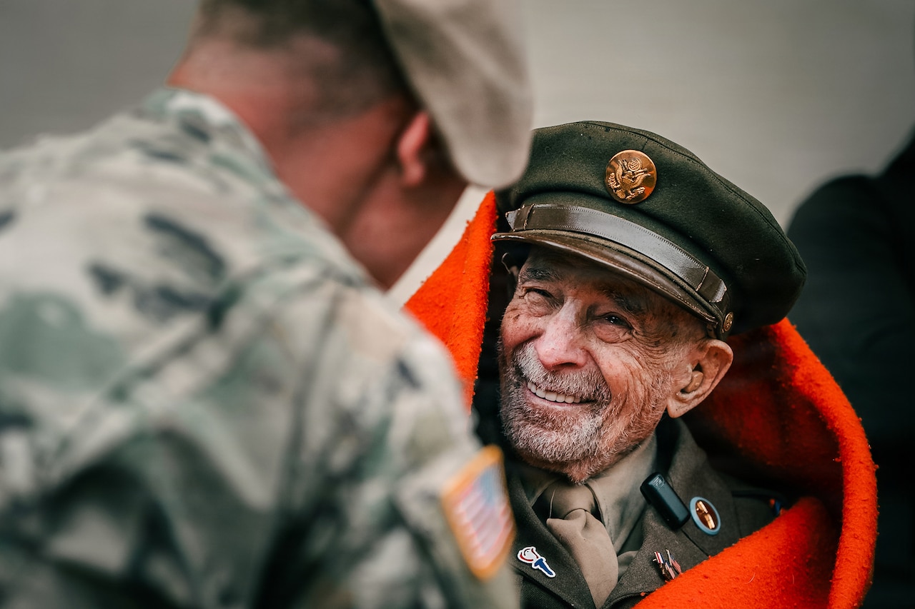 A smiling veteran in uniform speaks to a soldier.