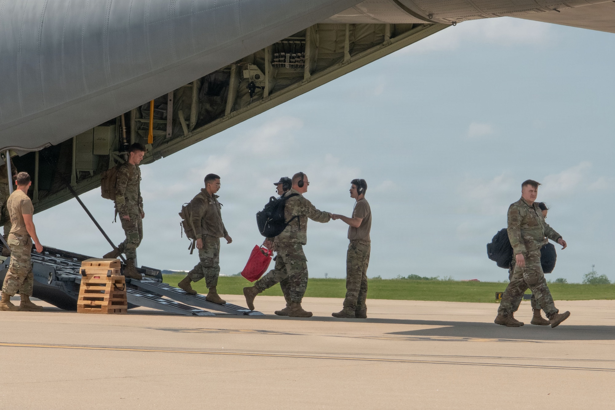 Uniformed members greet each other as some walk off an aircraft on a flightline.