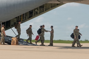 Uniformed members greet each other as some walk off an aircraft on a flightline.
