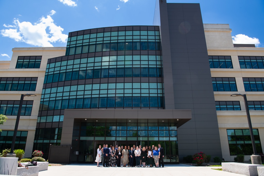 A group of people stand outside in front of a large building posing for a group photo.