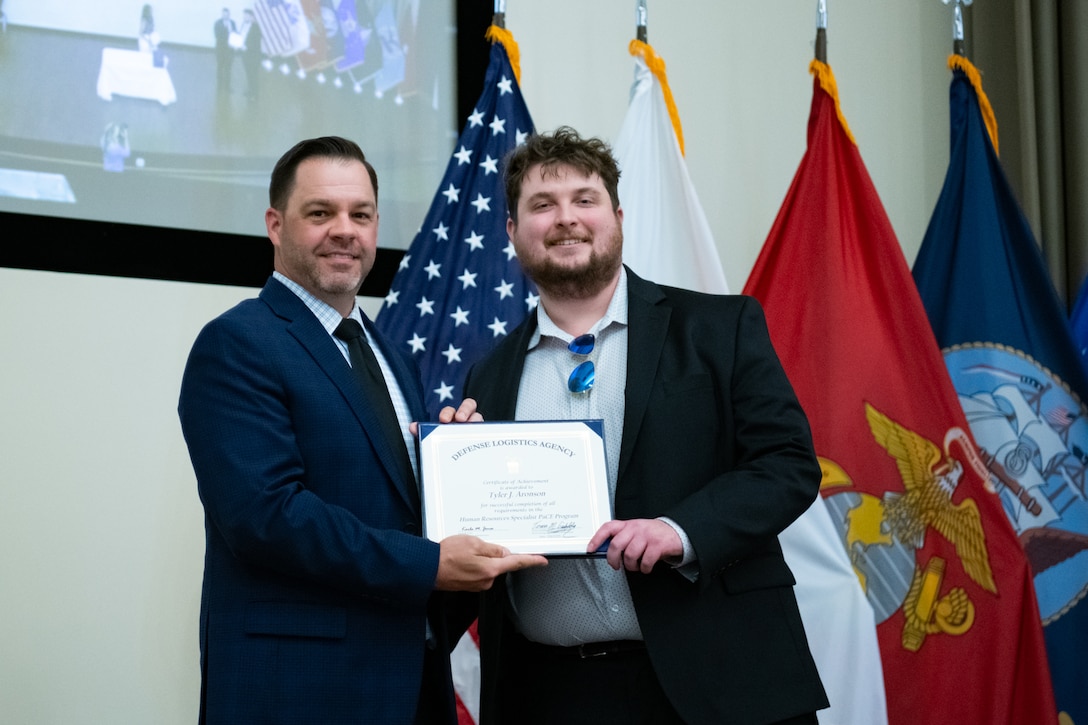 People stand indoors on a stage holding a certificate.