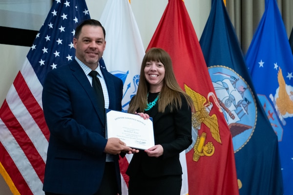 People stand indoors on a stage holding a certificate.