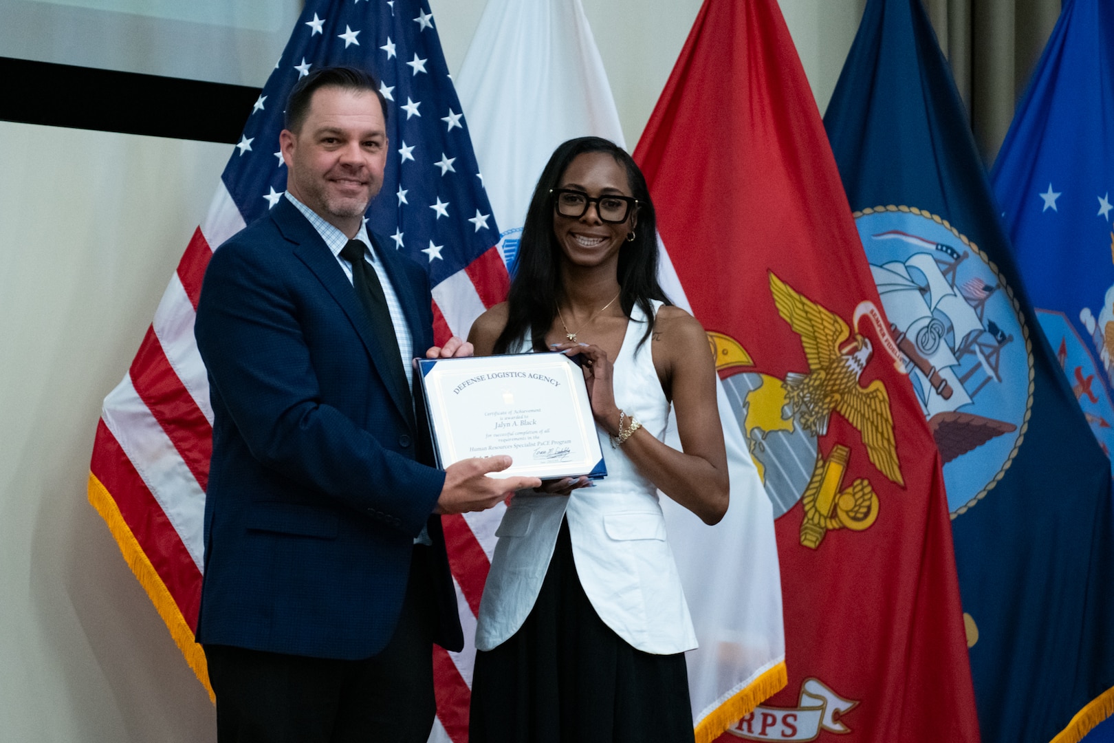 People stand indoors on a stage holding a certificate.