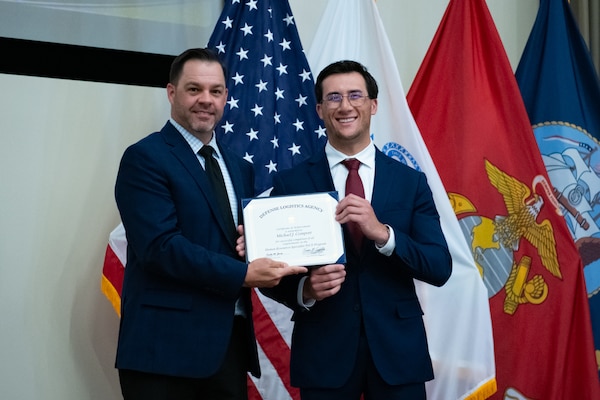 People stand indoors on a stage holding a certificate.