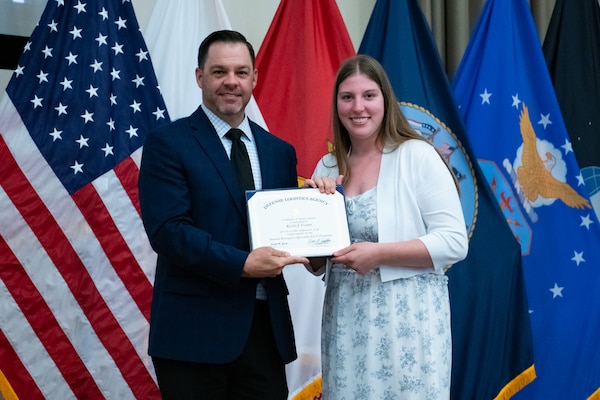 People stand indoors on a stage holding a certificate.