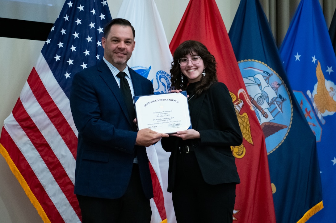 People stand indoors on a stage holding a certificate.