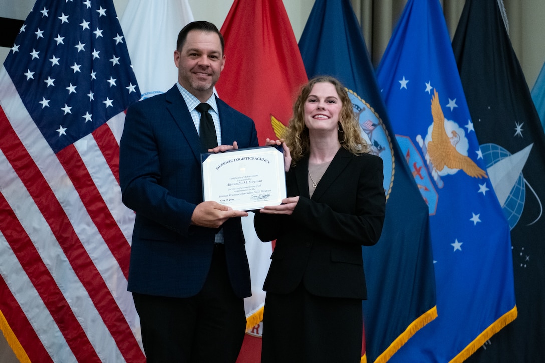 People stand indoors on a stage holding a certificate.