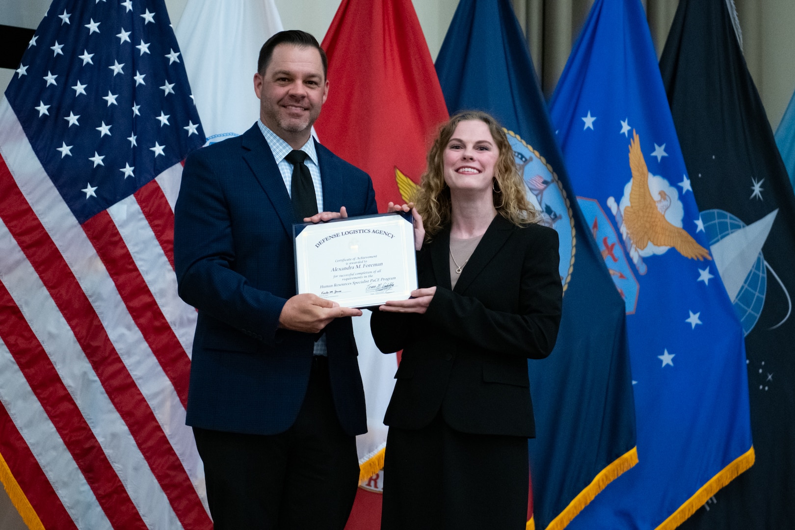 People stand indoors on a stage holding a certificate.