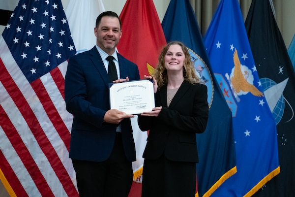 People stand indoors on a stage holding a certificate.