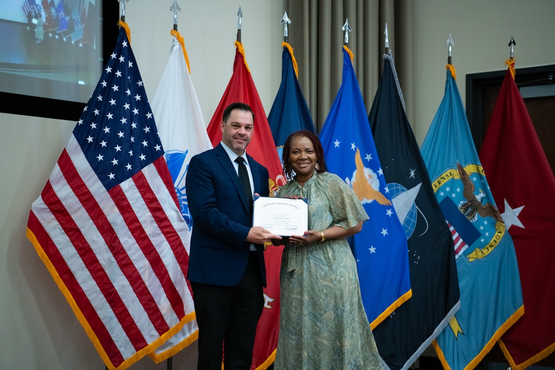 People stand indoors on a stage holding a certificate.