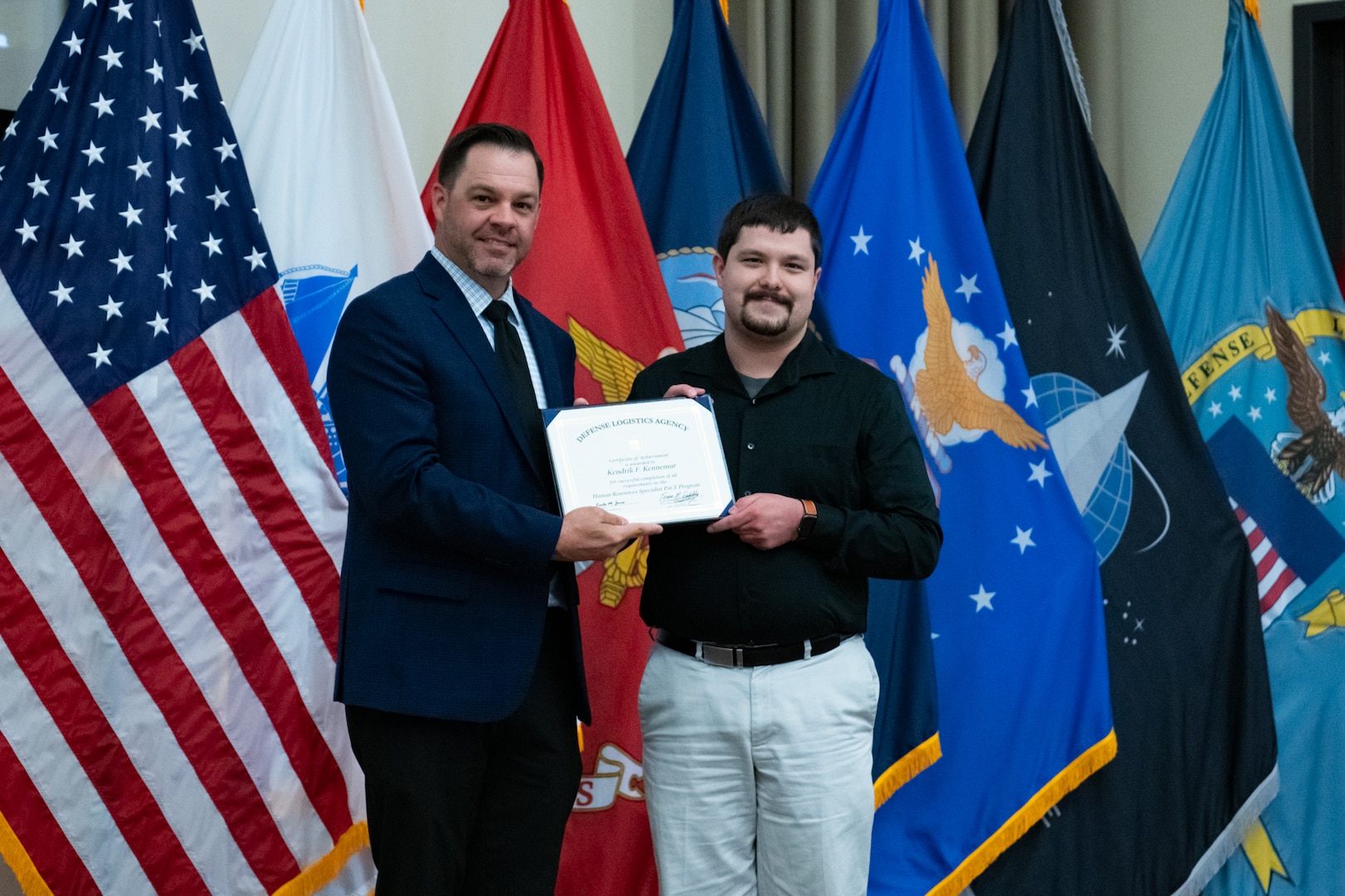 People stand indoors on a stage holding a certificate.