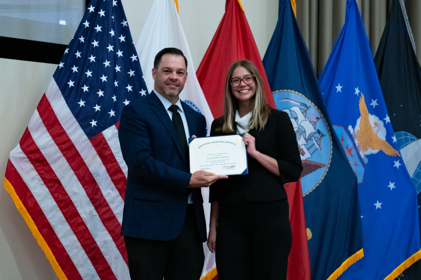 People stand indoors on a stage holding a certificate.