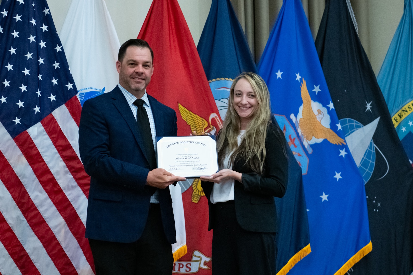 People stand indoors on a stage holding a certificate.
