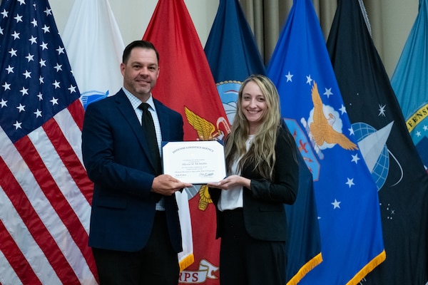 People stand indoors on a stage holding a certificate.