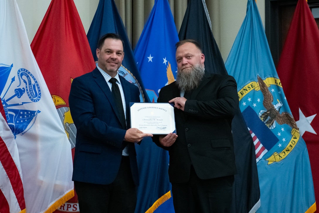 People stand indoors on a stage holding a certificate.