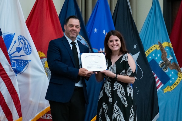 People stand indoors on a stage holding a certificate.