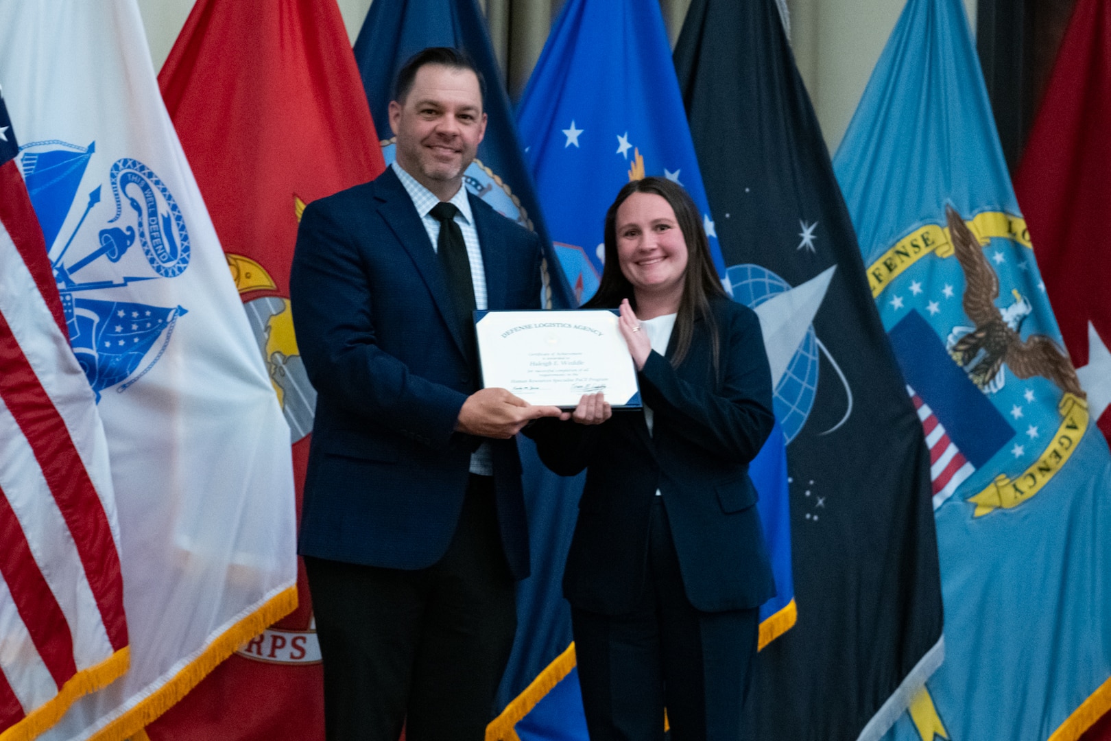 People stand indoors on a stage holding a certificate.