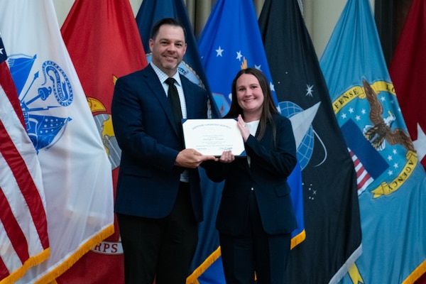 People stand indoors on a stage holding a certificate.