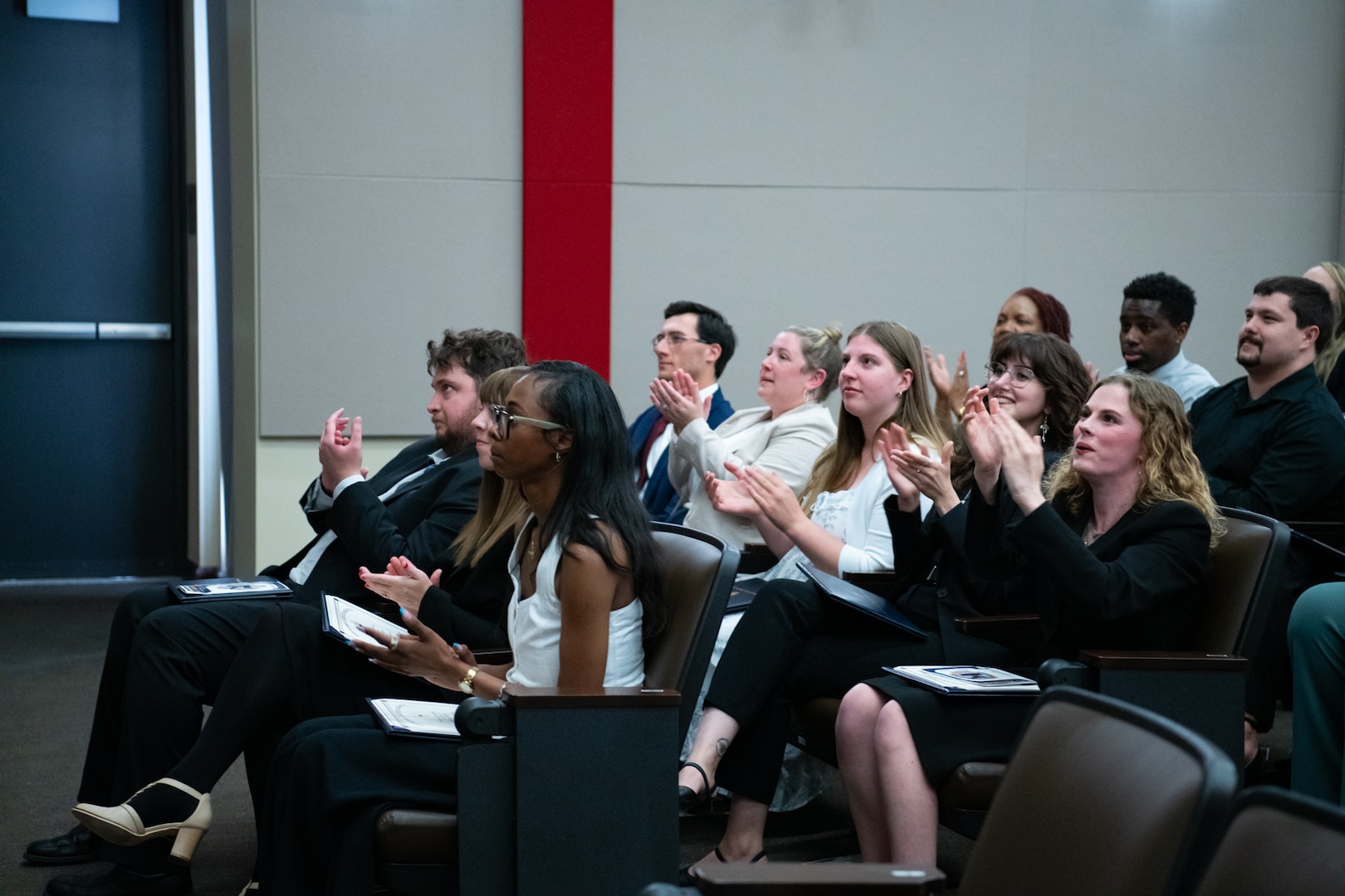 A group of people sit inside an auditorium clapping.