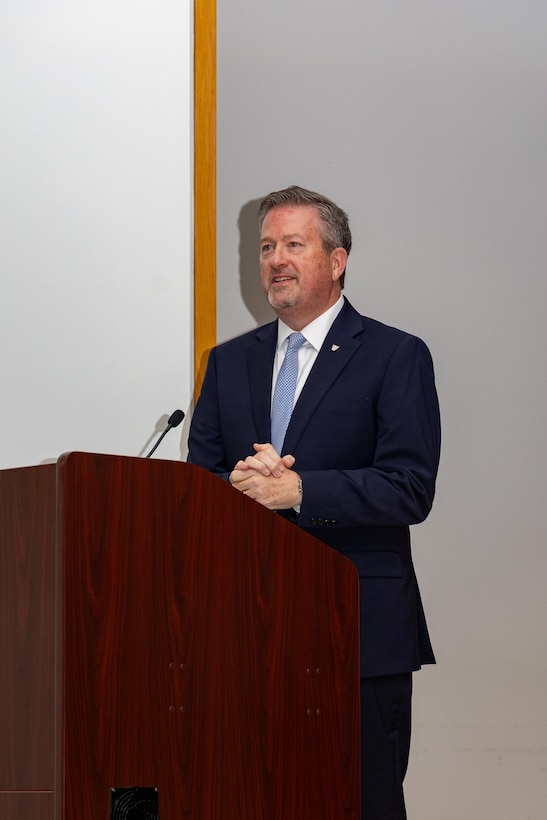 A man wearing a suit stands behind a podium speaking.