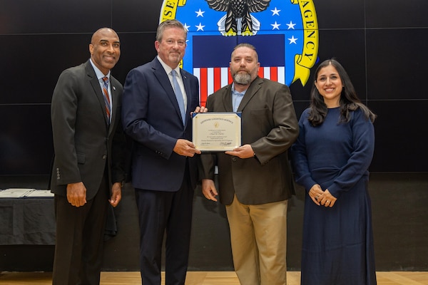 People stand indoors on a stage holding a certificate.