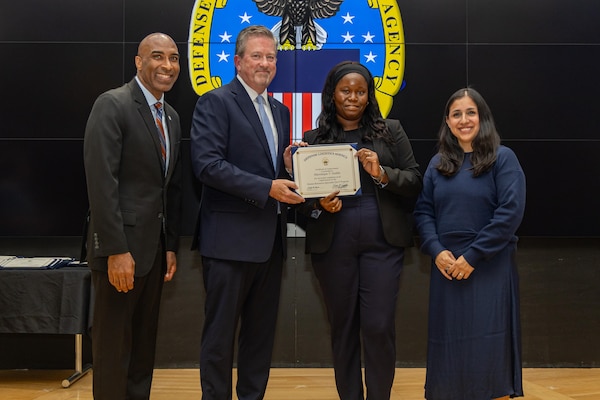 People stand indoors on a stage holding a certificate.