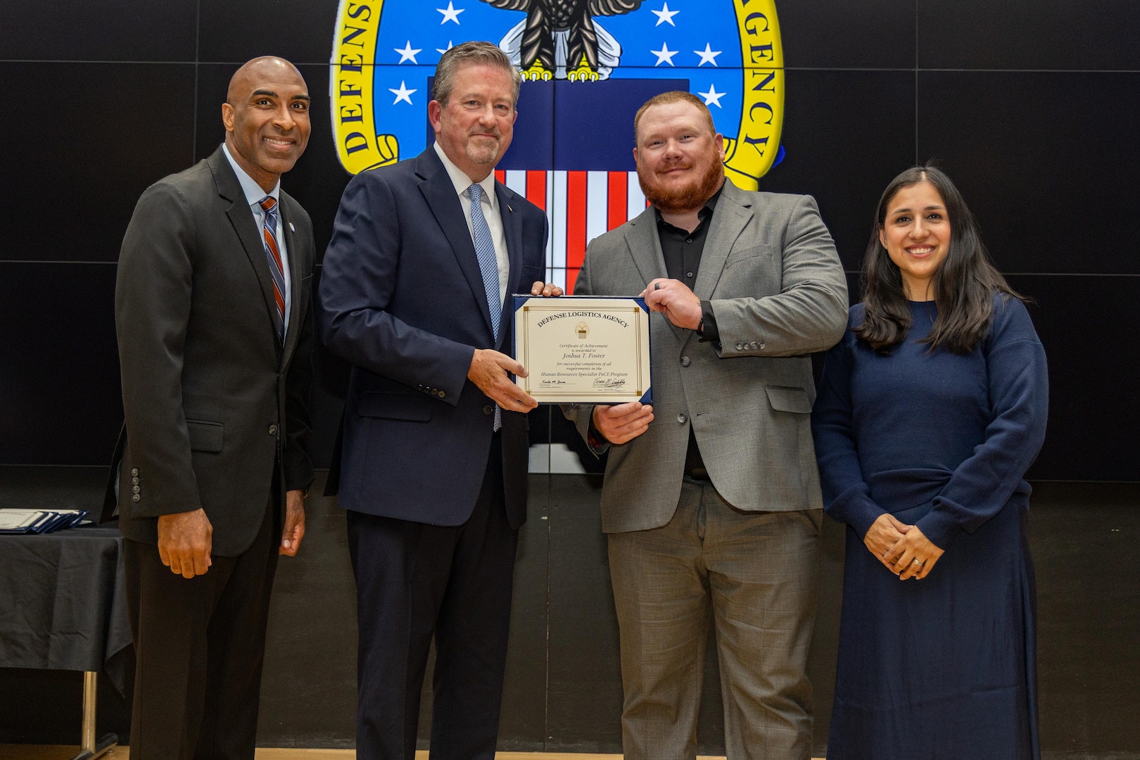 People stand indoors on a stage holding a certificate.